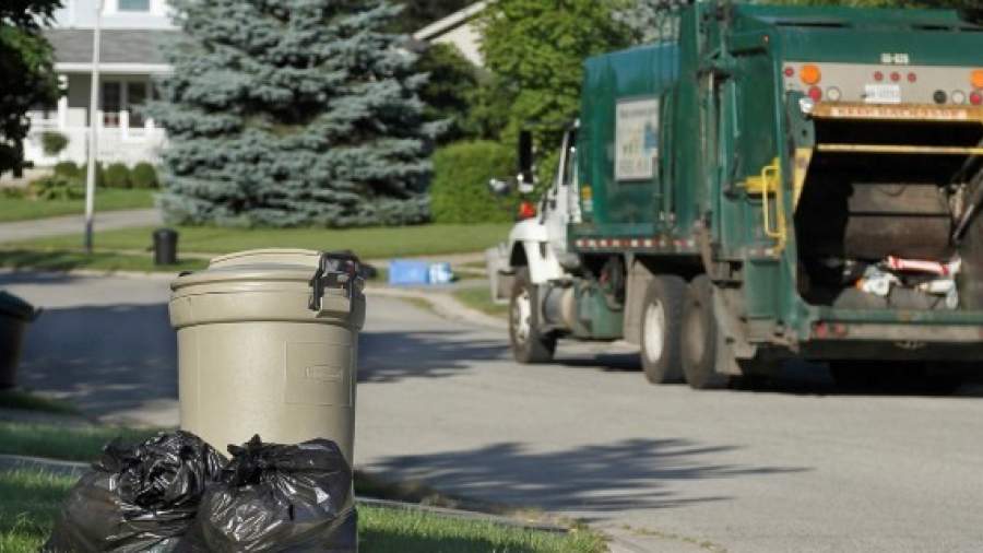 A garbage truck drives down a residential street with garbage containers placed at the curb. 