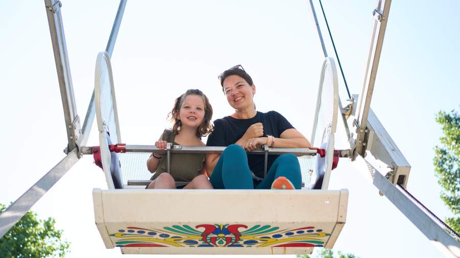 An adult and a child sit in a Ferris wheel seat smiling.